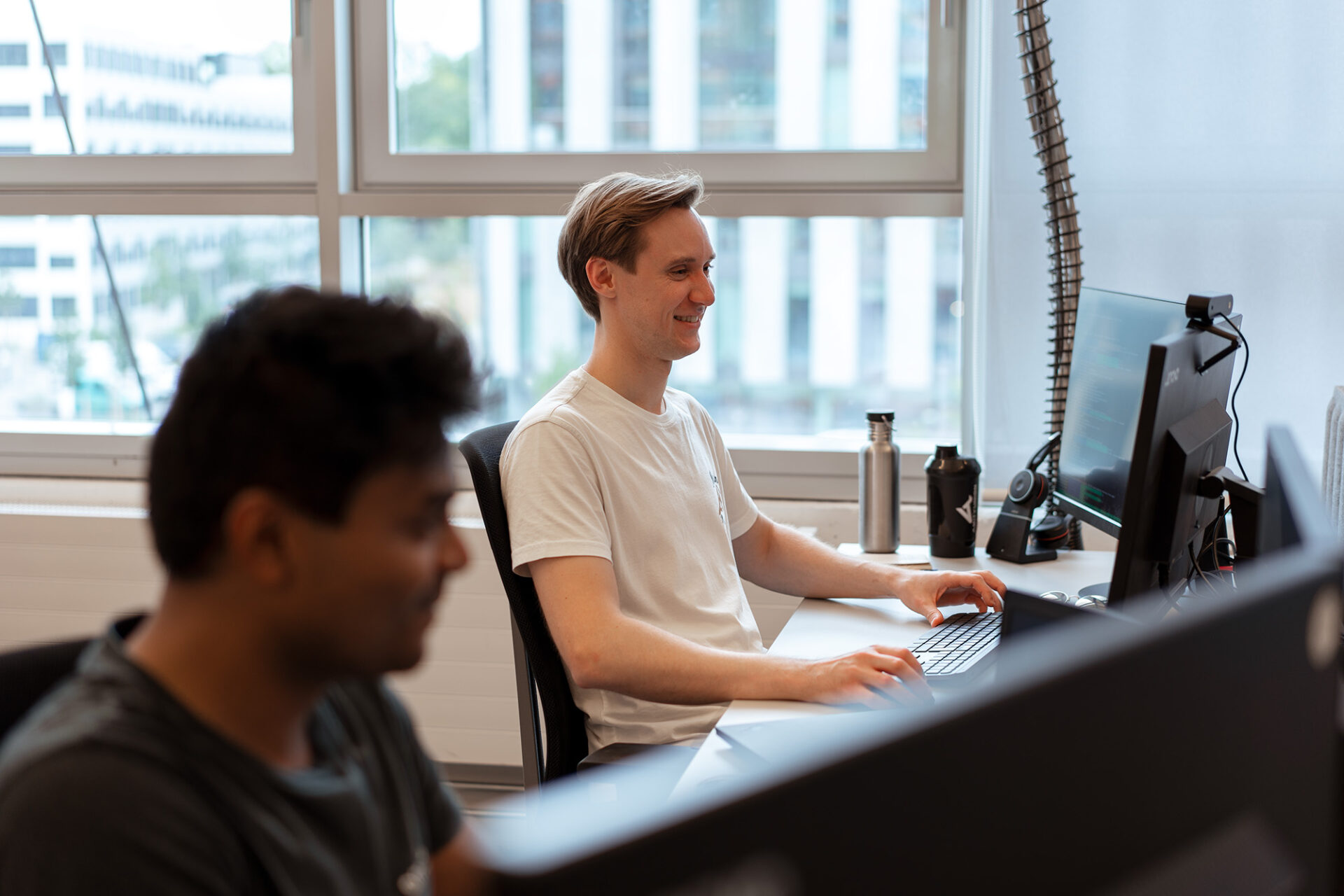 Two developers sitting next to each other at the arculus offce. They are both looking at their computer screens.