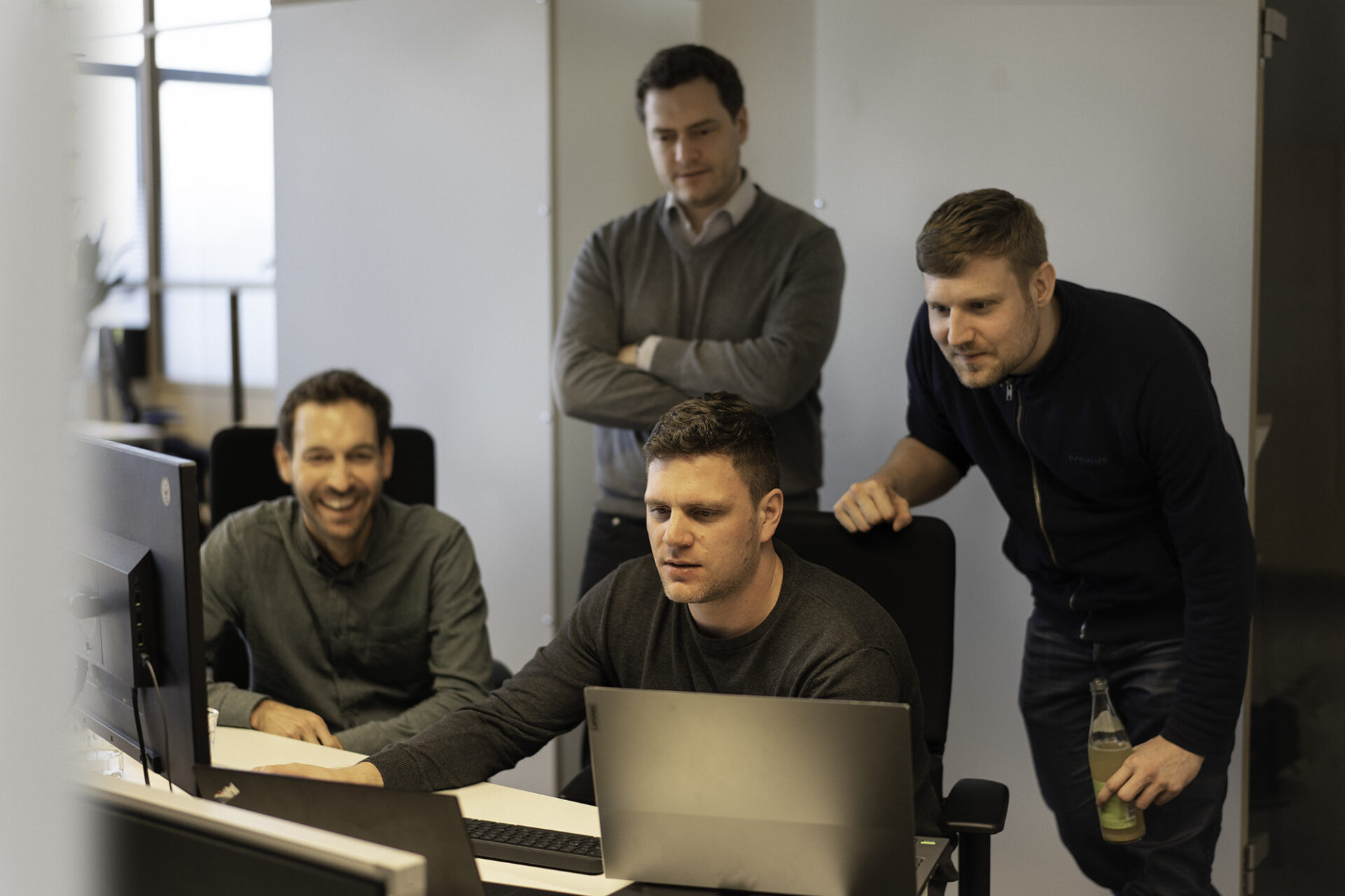 Four developers of different teams stare at a computer screen together. Cross-team collaboration helps arculus achieve fast development.