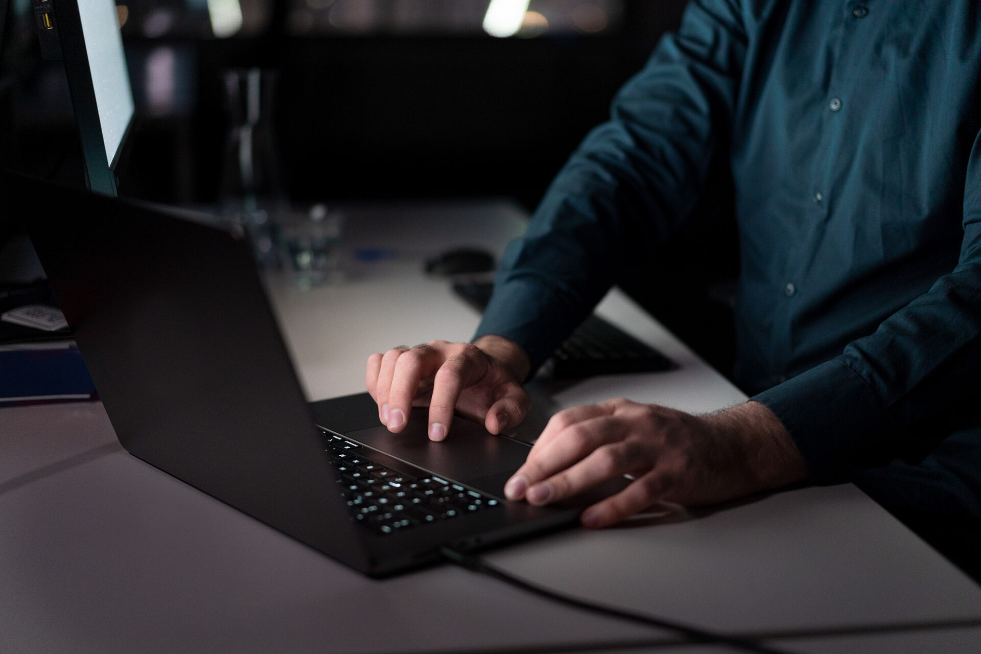 Night scene showing a developer sitting in front of a laptop. Only his torso is visible. He is wearing a dark blue shirt and sitting to the right of the image. His hands are illuminated by the light coming from the laptop.