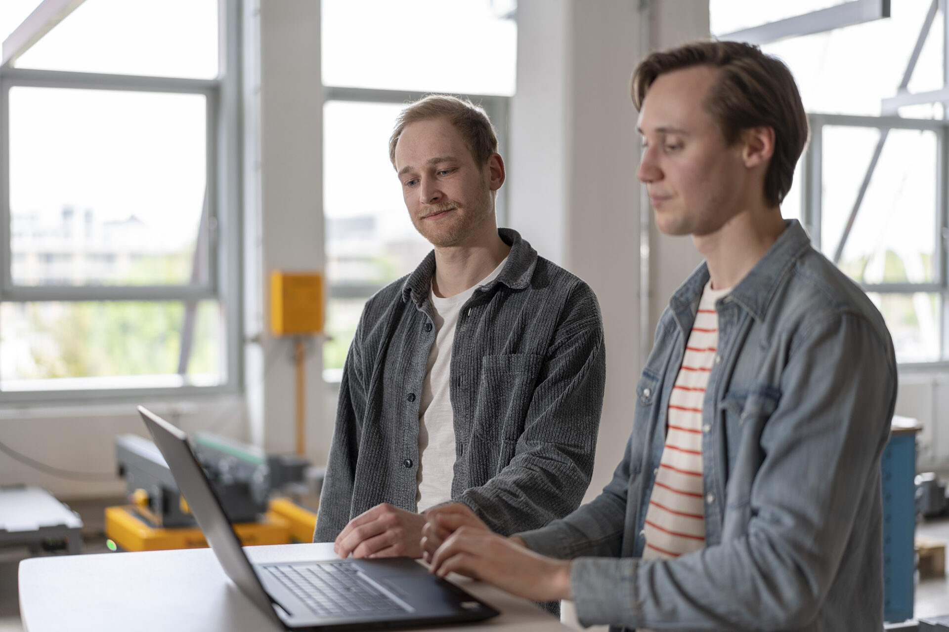 Two engineers looking at the same computer screen. Behind them, a few arculees can be seen.