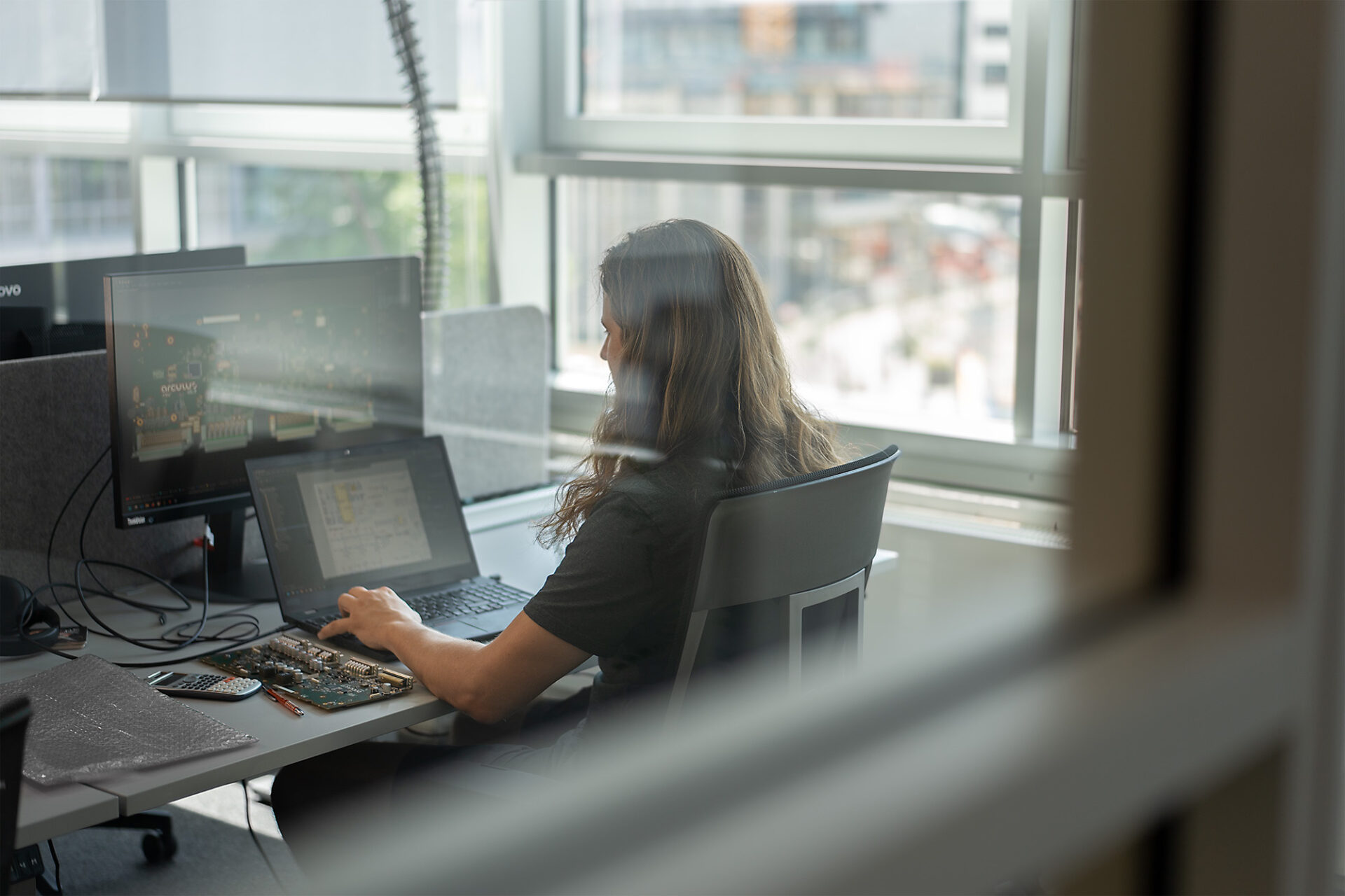 Tobias working at a desk in front of a window. There are two computers on the desk, one laptop and one monitor. To his left is the RCU®.