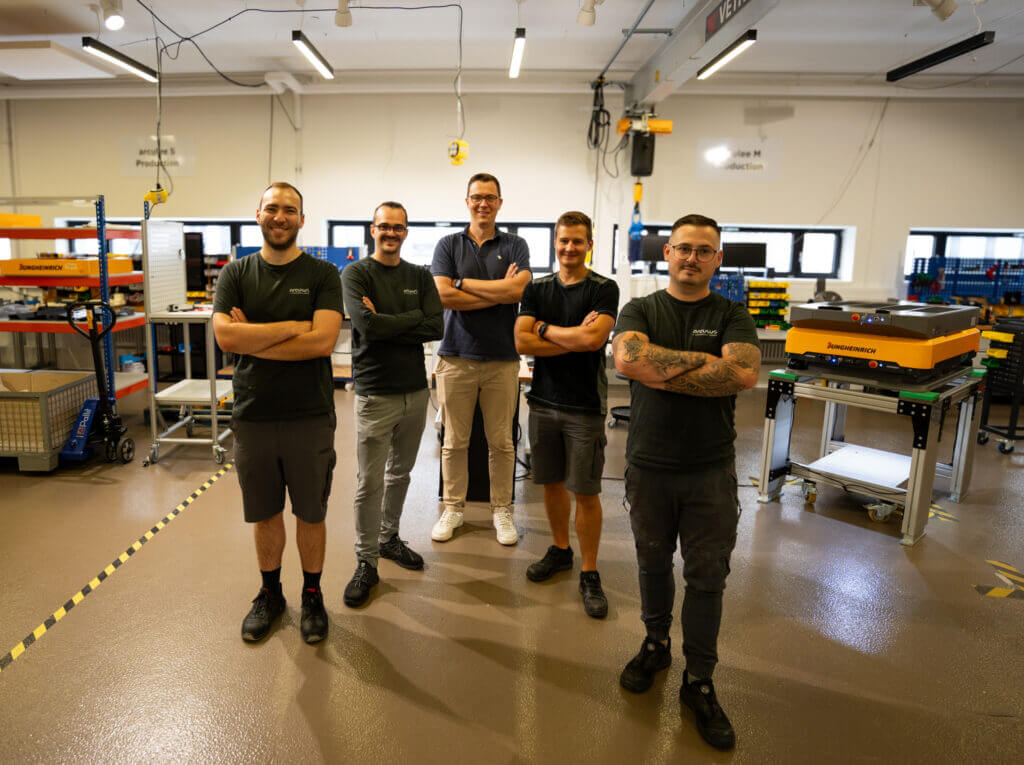 Five members of the arculus production team standing with arculee M (AMR) in the background