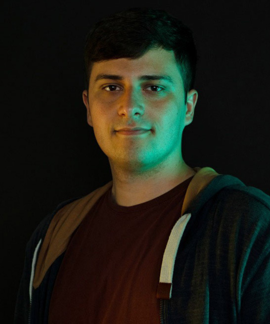 Iuri is a software engineer at arculus. He is looking at the camera. He has a green light shining on the right side of his face and a yellow light shining on the other side.