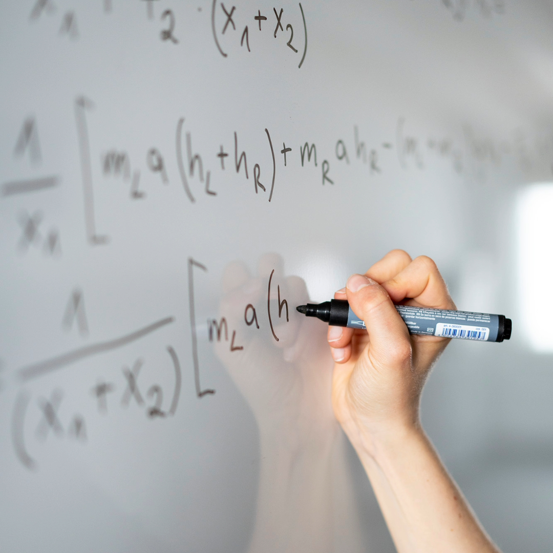 A photo of an engineer doing some calculations on a white board. You can see her hand while she writes some formulas.