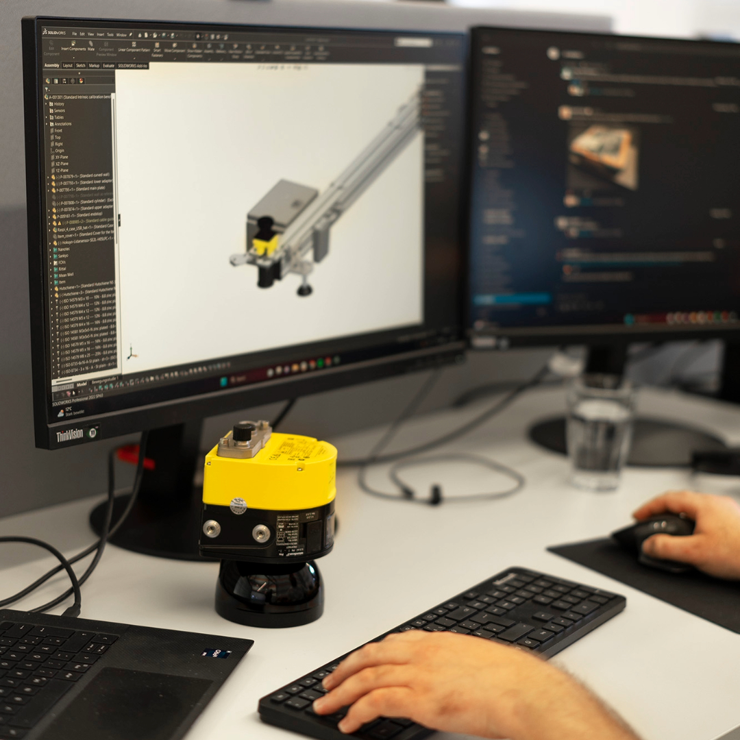 One of our engineers working on a CAD design for an arculee M part. You can see his hands on his keyboard along with the design on his screen and a 3D printed model below the computer.