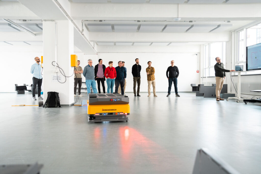 One person explains how to operate arculees (our AMRs) while several other people from the arculus stand and listen. An arculee is also visible in the frame. 